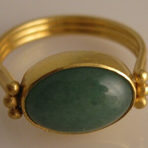 May include: A gold ring with a green oval gemstone set in a bezel setting. The band is decorated with three small gold balls.