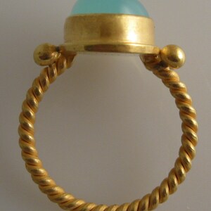 May include: A gold ring with a twisted band and a light blue cabochon gemstone set in a gold bezel.