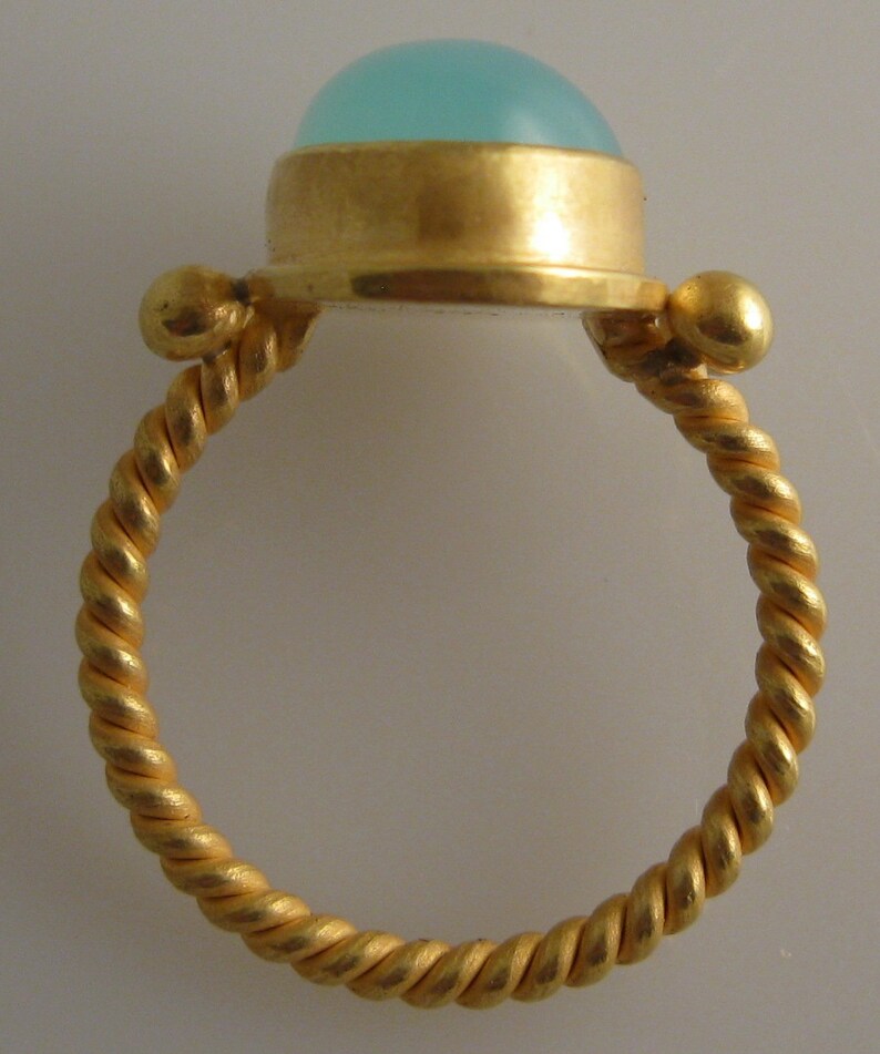 May include: A gold ring with a twisted band and a light blue cabochon gemstone set in a gold bezel.