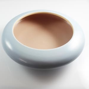Puede incluir: Un cuenco de cerámica azul claro con un borde liso y redondeado y un borde interior ligeramente más oscuro. El cuenco está vacío y tiene un acabado brillante.