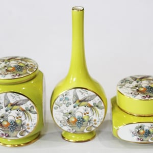 May include: A set of three yellow ceramic containers with gold trim and floral designs featuring birds and fruit. The set includes a vase and two jars with lids.
