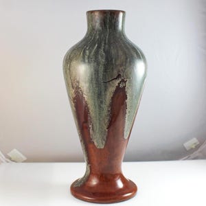 May include: A tall, decorative vase with a flared base and a slender neck. The vase features a color scheme of brown, green, and gray, with a glossy finish. The design has a dripped effect, adding to its unique aesthetic.