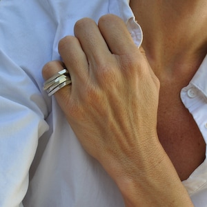 Puede incluir: Un anillo de plata con un diseño geométrico. El anillo está hecho de tres bandas que están apiladas una encima de la otra.