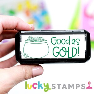 May include: A black and white self-inking stamp with a green pot of gold illustration and the text "Good as GOLD!"