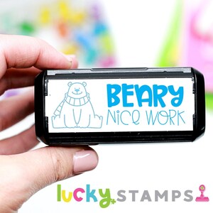 May include: A black and white self-inking stamp with a blue polar bear wearing a scarf and the text "Beary Nice Work".