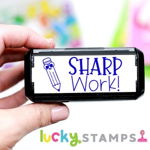 May include: A black and white self-inking stamp with a blue cartoon pencil and the text "SHARP Work!"