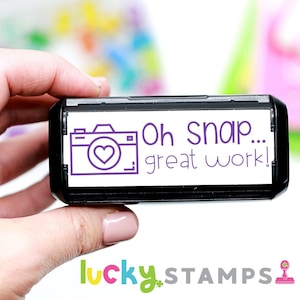 May include: A black and white self-inking stamp with a purple camera icon and the text "Oh Snap... great work!"