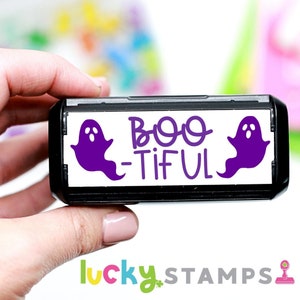 May include: A black and white self-inking stamp with two purple ghost illustrations and the text "Boo-tiful".