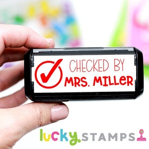 May include: Black and white self-inking stamp with a red checkmark and the text "CHECKED BY MRS. MILLER".