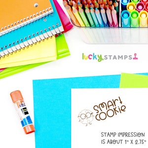 May include: A colorful collection of school supplies, including notebooks, colored pencils, markers, and a glue stick. A stamp with the text "Smart Cookie" and a cookie character is also visible. The stamp impression is about 1" x 2.75".