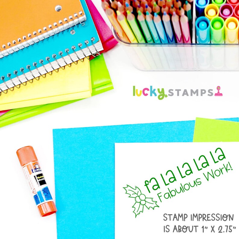 以下が含まれることがあります： 緑色の自己インク式のスタンプで、ヒイラギのデザインと「fa la la la la Fabulous Work!」というテキストが刻印されています。スタンプの印影は約2.5cm x 7cmです。