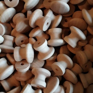 May include: A close-up of a pile of wooden knobs. The knobs are all round and have a small hole in the center. They are a light brown color and have a smooth finish.