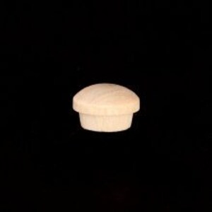 May include: A single, unfinished wooden furniture plug with a rounded top and a cylindrical base. The plug is light brown in color and appears to be made of a softwood. The background is solid black.