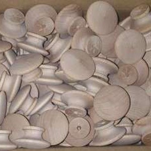 May include: A box filled with wooden knobs, each with a round top and a small hole in the center. The knobs are a light brown color and have a smooth finish.