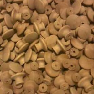 May include: A large pile of unfinished wooden knobs. The knobs are round with a small cylinder in the center. The knobs are a light brown color.