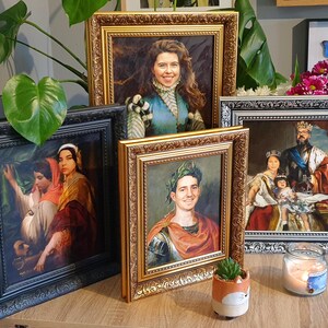 May include: Four framed portraits of people in different historical costumes. The portraits are in gold, black, and silver frames. The frames are ornate and have a decorative design. The portraits are on a wooden table with a small potted plant and a candle.