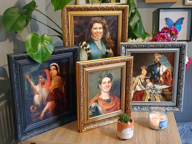 May include: Four framed portraits of people in different historical costumes. The portraits are in gold, black, and silver frames. The frames are ornate and have a decorative design. The portraits are on a wooden table with a small potted plant and a candle.