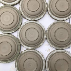 May include: A collection of eight ceramic plates, each with a slightly different shade of brown, are arranged in a circular pattern on a white surface. The plates are all the same size and have a smooth, glazed finish.