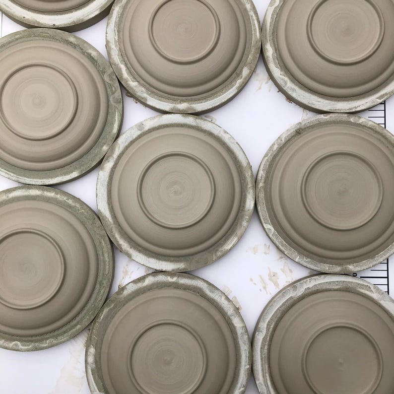 May include: A collection of eight ceramic plates, each with a slightly different shade of brown, are arranged in a circular pattern on a white surface. The plates are all the same size and have a smooth, glazed finish.