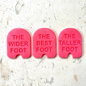 May include: Three pink plastic foot-shaped markers with the text "The Wider Foot", "The Best Foot", and "The Taller Foot" printed on them.