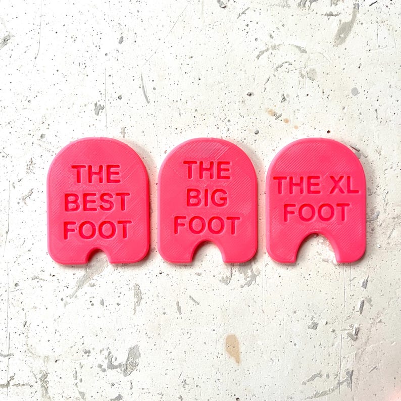 May include: Three pink plastic shoe inserts with the text "The Best Foot", "The Big Foot", and "The XL Foot" printed on them.