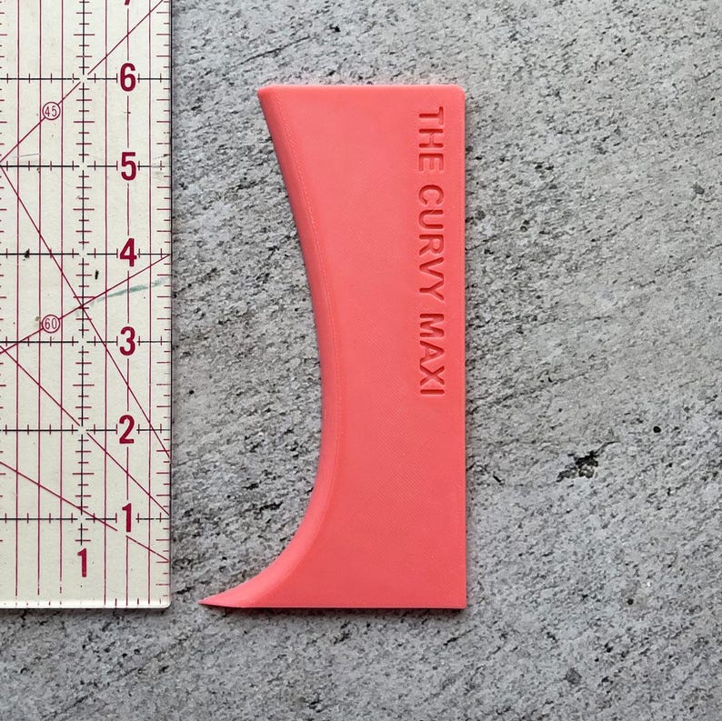 May include: A bright pink plastic tool called "The Curvy Maxi" for smoothing out fondant or icing.