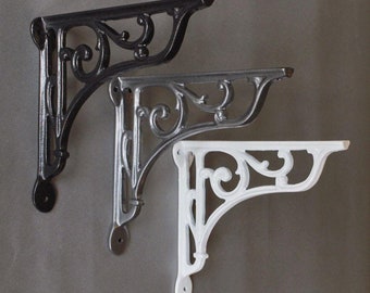 May include: Three decorative shelf brackets in different finishes: black, silver, and white. Each bracket features a scrolled design.