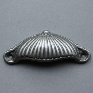May include: A silver metal cabinet pull with a fluted design. The pull has a rounded top and two small holes on either side.