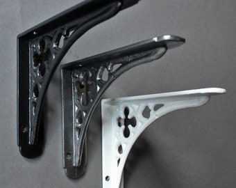May include: Three decorative shelf brackets, two black and one white, with a decorative, ornate design. The brackets are made of cast iron and have a traditional style.