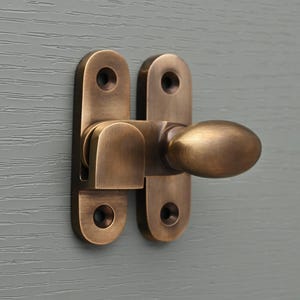 May include: A brushed brass door latch with an oval-shaped handle. The latch is mounted on a gray surface.