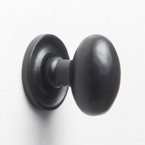 May include: Black cabinet knob with a round, slightly oval-shaped design. The knob has a smooth, matte finish.