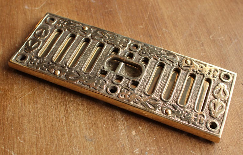 May include: A brass vent cover with a decorative design of leaves and flowers. The vent cover has a rectangular shape and is approximately 10 inches long.