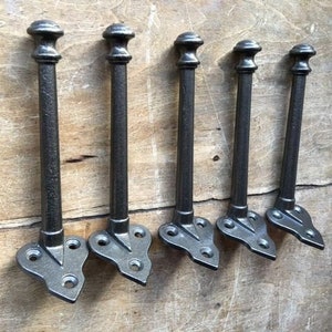 Könnte beinhalten: Fünf schwarze Metallhaken mit einer spitzen Spitze und einem dekorativen Design. Die Haken sind auf einer Holzoberfläche montiert.