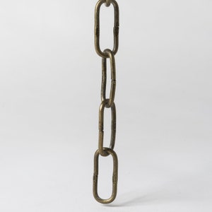 May include: Close-up of a section of a brass-colored chain against a white background. The chain links are oval-shaped and connected, with a slightly textured surface. The chain is likely for a lamp or other hanging fixture.