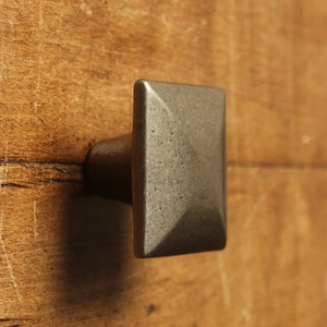 Peut inclure: Un bouton de porte carré en étain avec une surface légèrement surélevée et texturée.