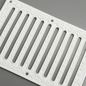 May include: White cast iron vent cover with an ornate design. The cover has nine vertical slots and a decorative border.
