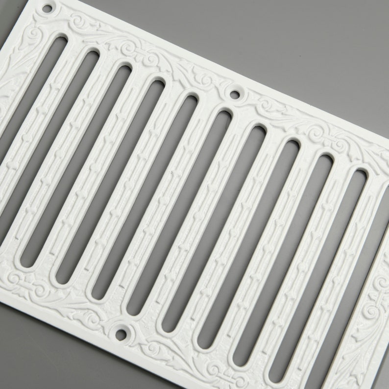 May include: White cast iron vent cover with an ornate design. The cover has nine vertical slots and a decorative border.