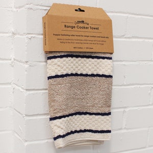 May include: A beige and white striped kitchen towel with a blue border. The towel is hanging from a brown cardboard package that says "Creative Mill Range Cooker Towel". The package says "Popper-fastening roller towel for range cookers and towel rolls. Makes a continuous towel loop which hangs out to dry without falling to the floor, keeping cleaner and dryer for longer. 85% Cotton + 15% Linen."