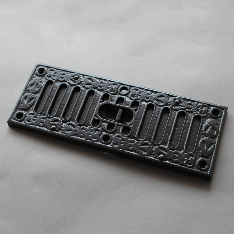 May include: Black cast iron vent cover with a decorative floral design and a rectangular opening.