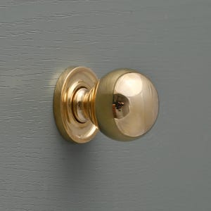 May include: A polished brass door knob with a round, spherical design. The knob is mounted on a round, flat base.