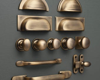 May include: A collection of antique brass cabinet hardware, including knobs, pulls, and drawer pulls. The hardware is arranged on a gray background.