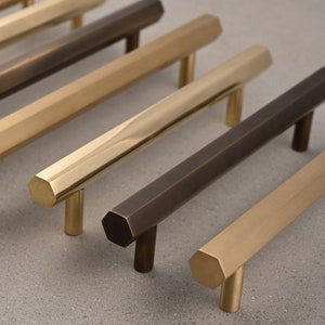 Può includere: Un set di cinque maniglie per armadi in diverse finiture, tra cui ottone, bronzo e nichel. Le maniglie sono esagonali e hanno un design moderno e minimalista.