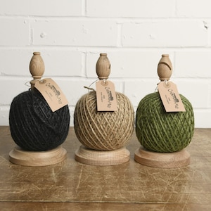 Puede incluir: Tres carretes de madera con ovillos de hilo en negro, natural y verde. Cada carrete tiene una perilla de madera y una etiqueta que dice "Creamore Mill Oak".