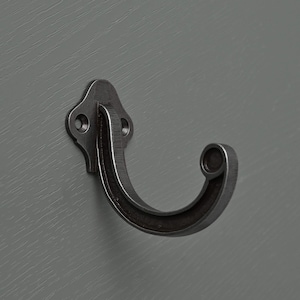May include: A silver metal hook with a decorative design. The hook is mounted on a gray wall.