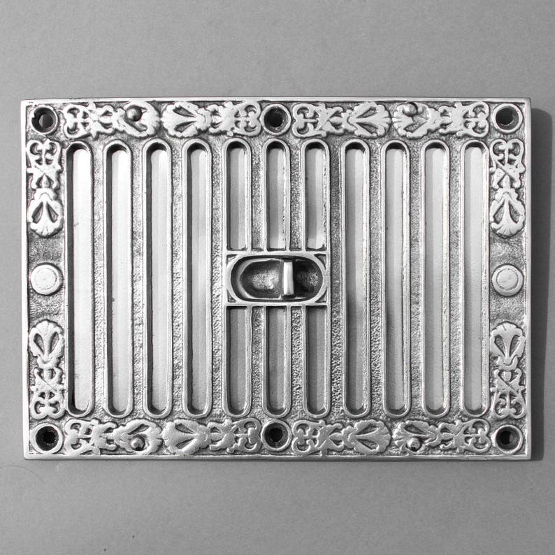 May include: A silver metal vent cover with a decorative border and a rectangular grille. The vent cover has a small, rectangular, metal damper.