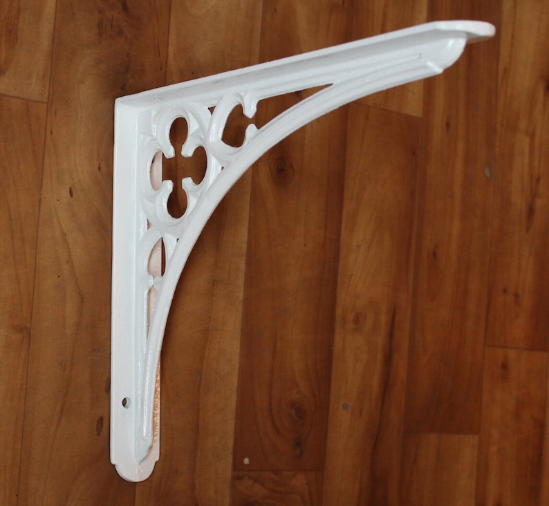 Puede incluir: Soporte de estante de metal blanco con un dise&ntilde;o decorativo y ornamentado. El soporte tiene forma de &aacute;ngulo recto y un borde festoneado.