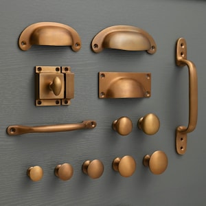 May include: A collection of antique brass cabinet hardware, including pulls, knobs, and a latch. The hardware is displayed on a gray background.