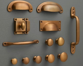 May include: A collection of antique brass cabinet hardware, including pulls, knobs, and a latch. The hardware is displayed on a gray background.