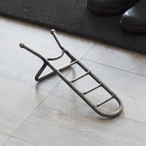 Puede incluir: Un calzador de metal con un diseño de escalera. El calzador está hecho de metal negro y tiene un mango redondeado.