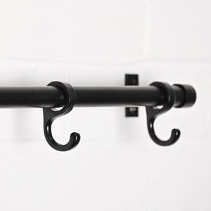 May include: A black metal rail with two curved hooks, mounted on a white brick wall. The hooks are designed to hold items, and the rail is attached to the wall with small, square brackets.